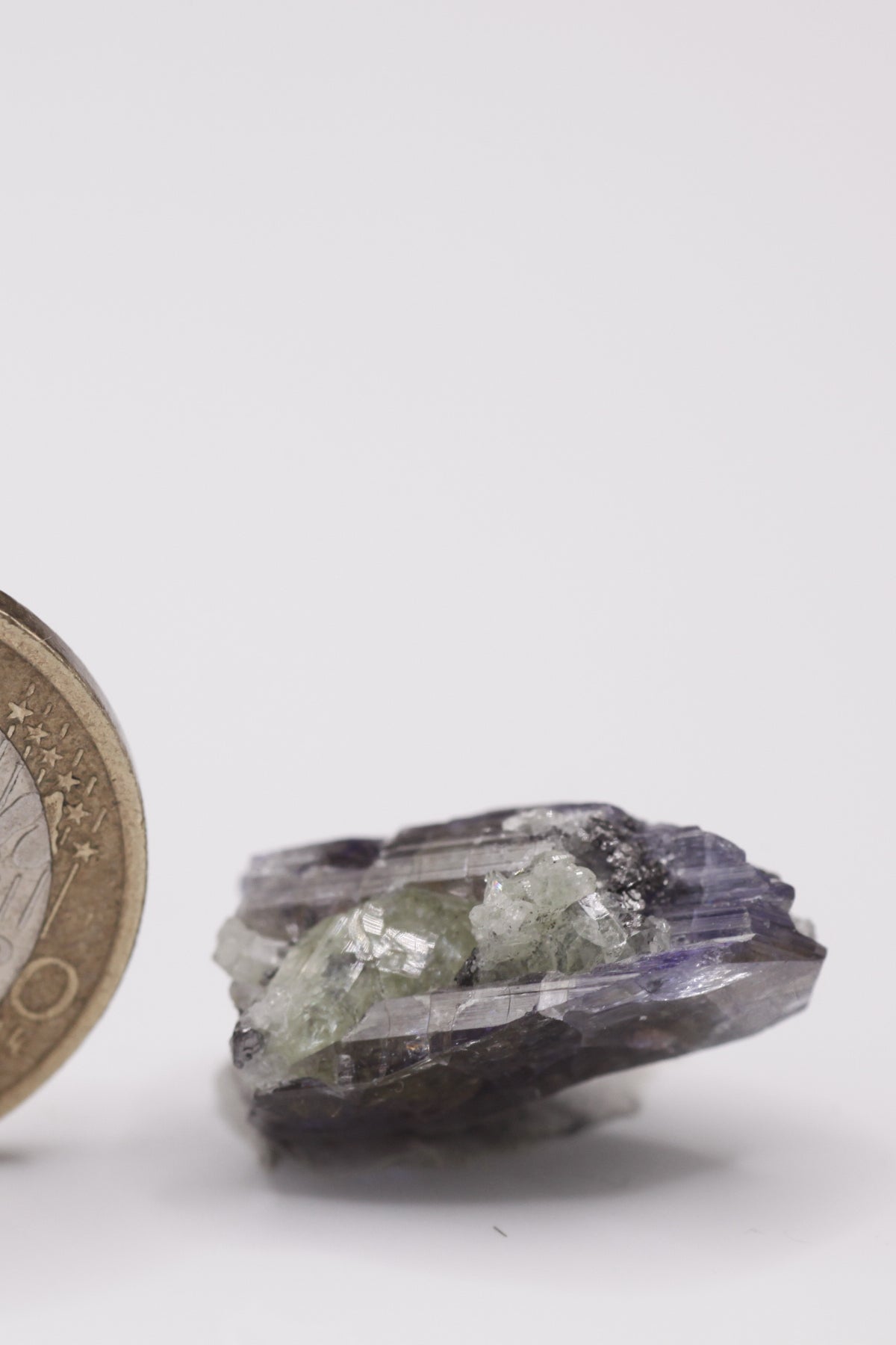 Tanzanite - Mine Mineral Market : A010 Ein sehr interessanter Tansanit-Kristall, seitlich sitzen Diopsidkristalle und etwas Graphit auf. Die untere Bruchfläche ist zum Teil verheilt. Sehr guter Glanz und Endfläche.