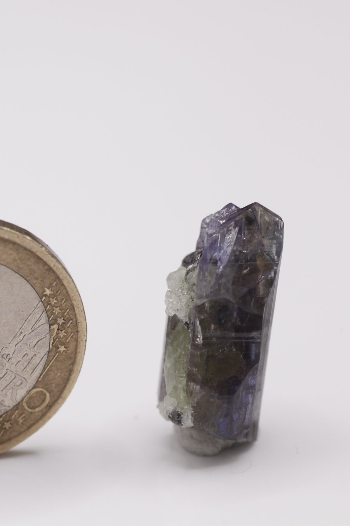 Tanzanite - Mine Mineral Market : A010 Ein sehr interessanter Tansanit-Kristall, seitlich sitzen Diopsidkristalle und etwas Graphit auf. Die untere Bruchfläche ist zum Teil verheilt. Sehr guter Glanz und Endfläche.