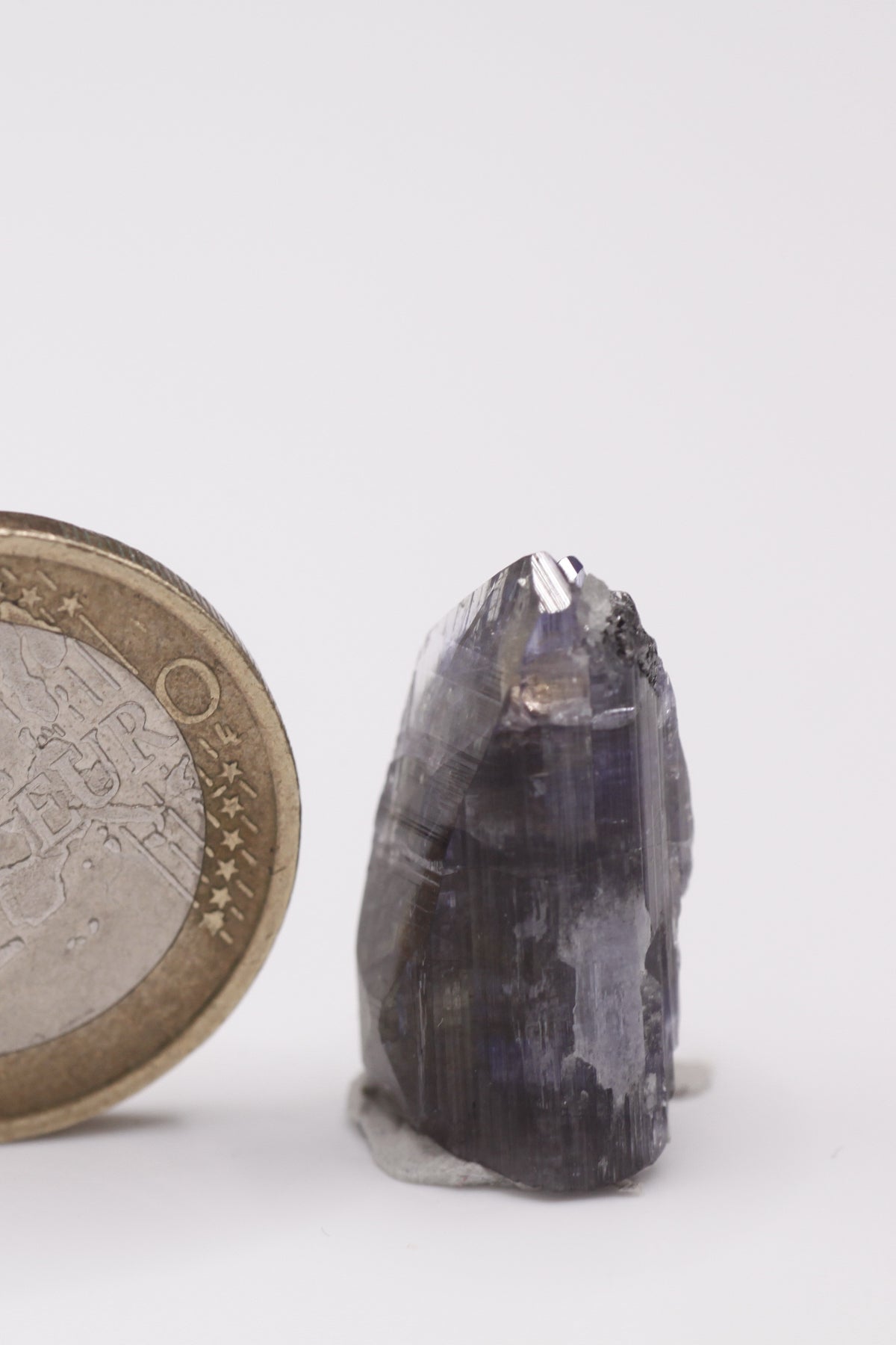 Tanzanite - Mine Mineral Market : A010 Ein sehr interessanter Tansanit-Kristall, seitlich sitzen Diopsidkristalle und etwas Graphit auf. Die untere Bruchfläche ist zum Teil verheilt. Sehr guter Glanz und Endfläche.