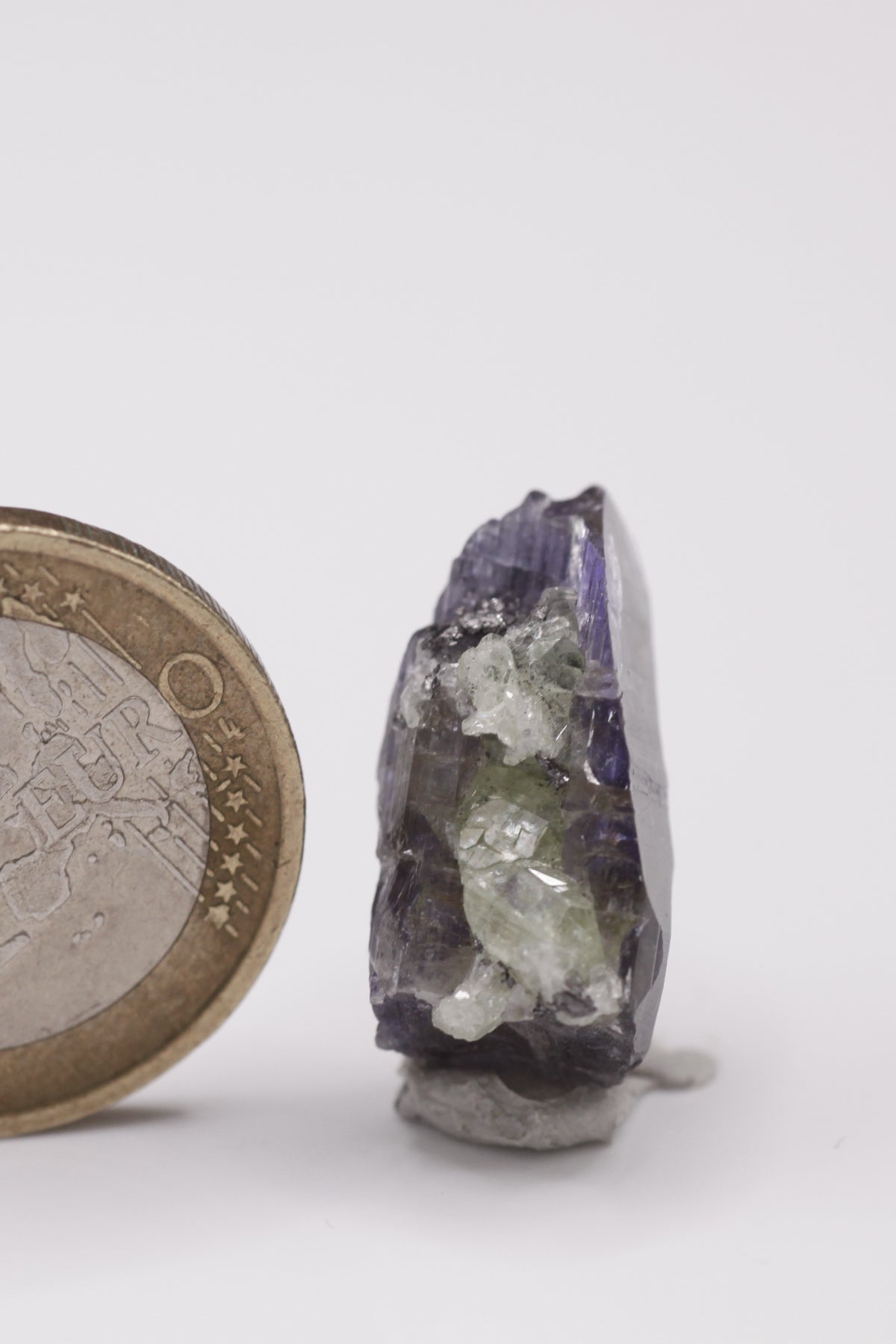 Tanzanite - Mine Mineral Market : A010 Ein sehr interessanter Tansanit-Kristall, seitlich sitzen Diopsidkristalle und etwas Graphit auf. Die untere Bruchfläche ist zum Teil verheilt. Sehr guter Glanz und Endfläche.
