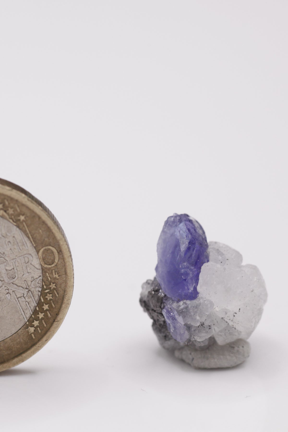 Tanzanite - Mine Mineral Market : A012 Ein kleiner blauer Tansanit-Kristall sitzt auf kugeligem weißen Prehnit-Aggregat. Eine kleine nette Stufe durch den Kontrast zu zusätzlich seitlich anhaftendem Graphit.