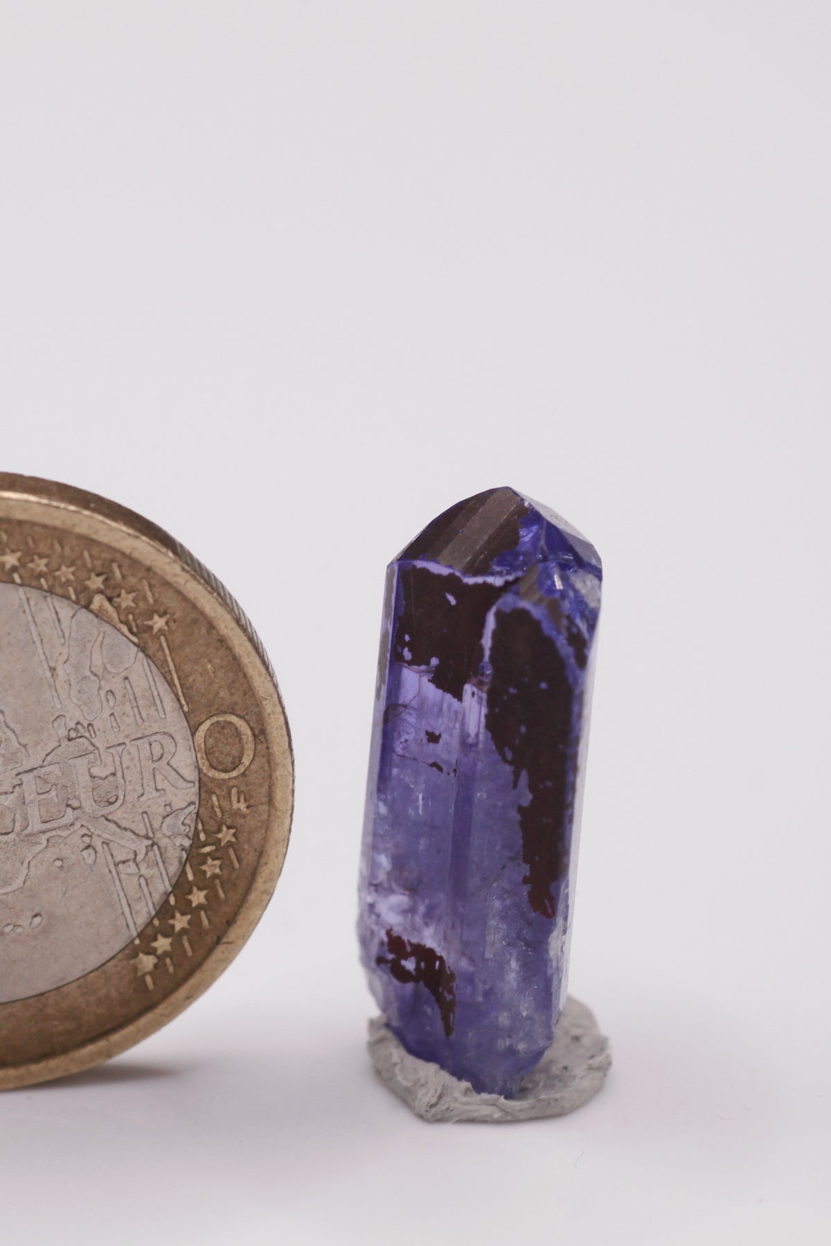 Tanzanite  - Mine Mineral Market :    A035 Ein vollständiger klarer Kristall (im oberen Teil von Facettierqualität) mit hervorragenden Endflächen, auf der Rückseite teilweise mit Alabandin überzogen, sonst sehr guter Glanz.
