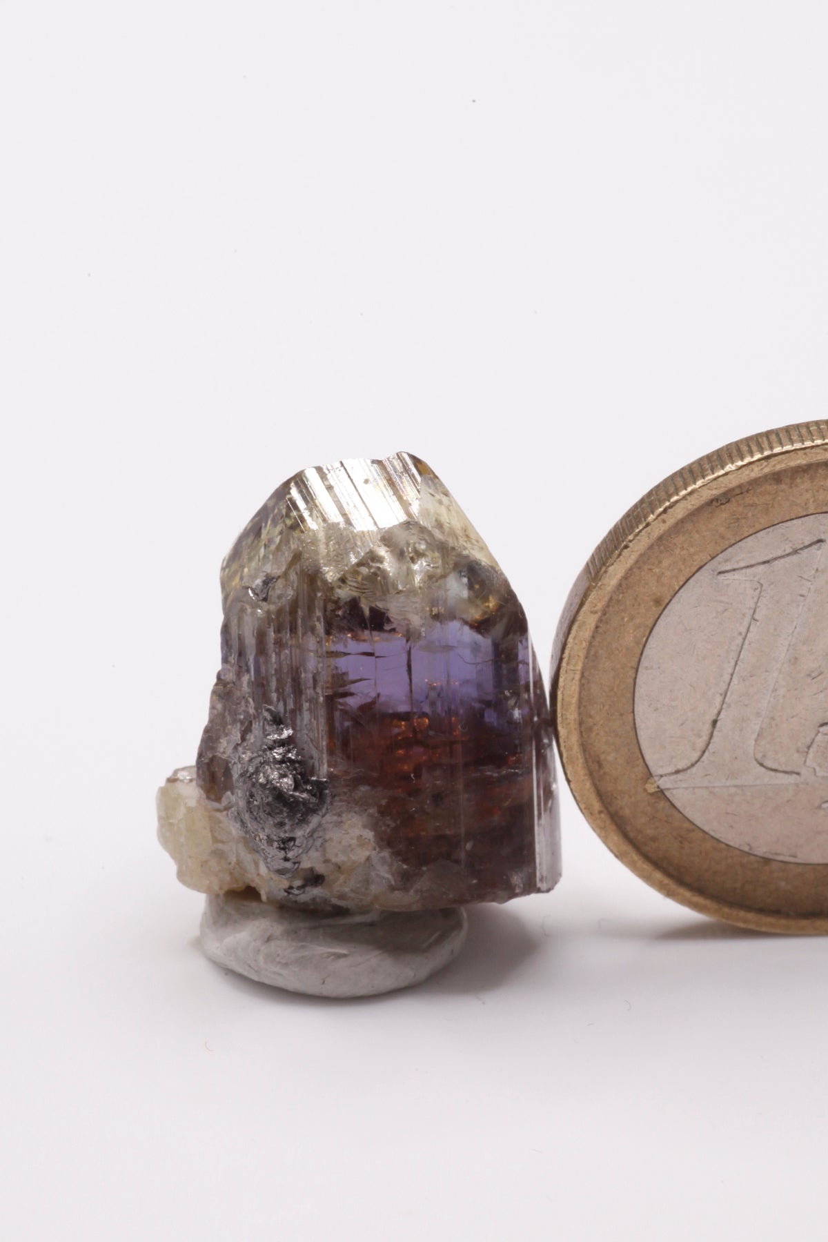 Tanzanite - Mine Mineral Market : A232 Wir erhielten ein Tansanitlot aus Altbeständen eines sightholders der seit 2015 geschlossenen Tanzanite One mining Gesellschaft. Dieser gut glänzende Kristall ist zweifarbig, oben gelb und in der Mitte klassisch grau bzw. blauviolett. An der Seite etwas Graphit und Diopsid sowie eine Beschädigung.