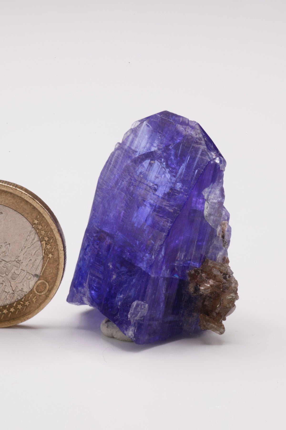 Tanzanite  - Mine Mineral Market :    A028 Ein größerer transparenter und unbeschädigter Kristall von schöner tiefblauer Farbe, mit etwas Matrix (Graphit & Diopsid) und sehr gutem Glanz.  