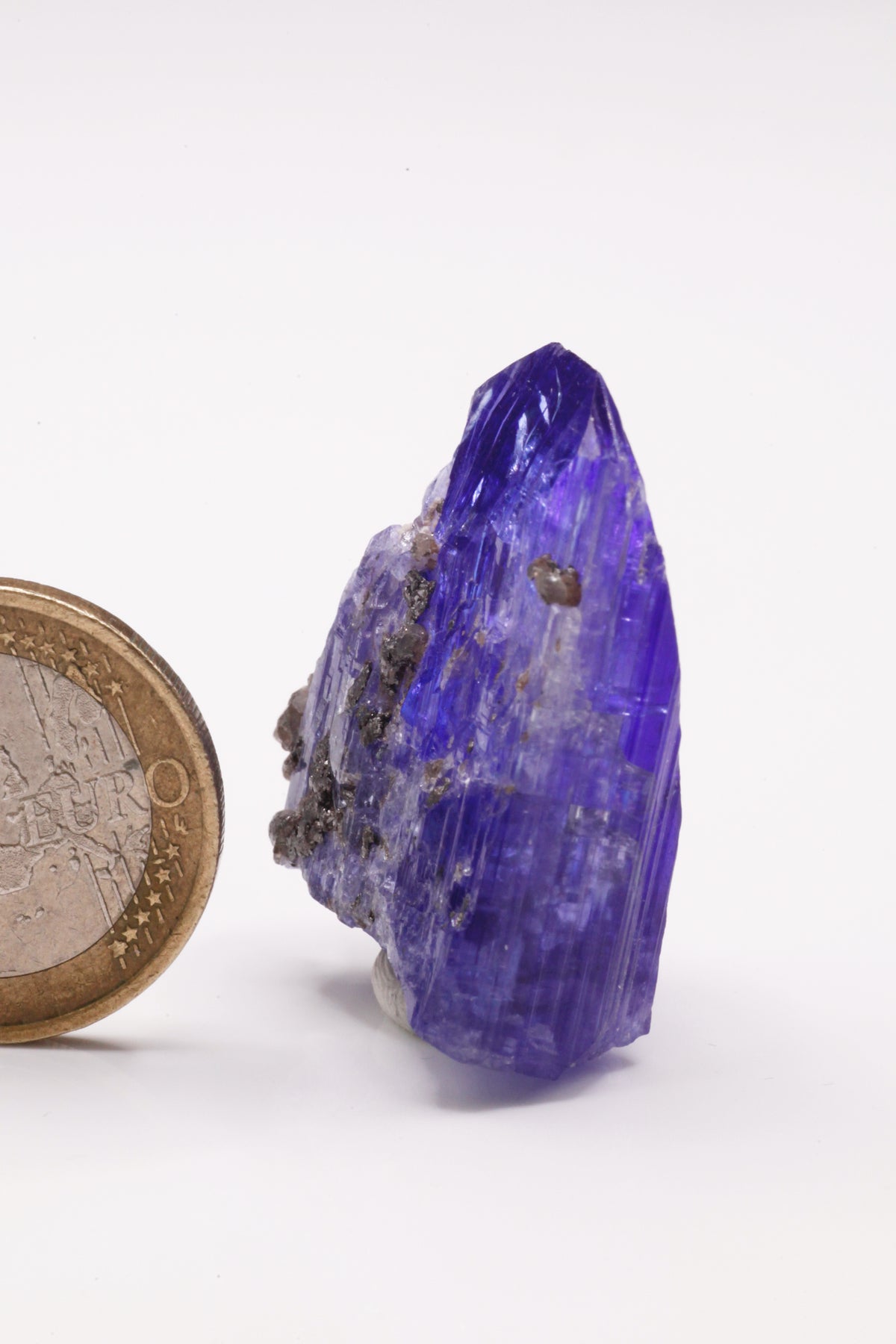 Tanzanite  - Mine Mineral Market :    A028 Ein größerer transparenter und unbeschädigter Kristall von schöner tiefblauer Farbe, mit etwas Matrix (Graphit & Diopsid) und sehr gutem Glanz.  