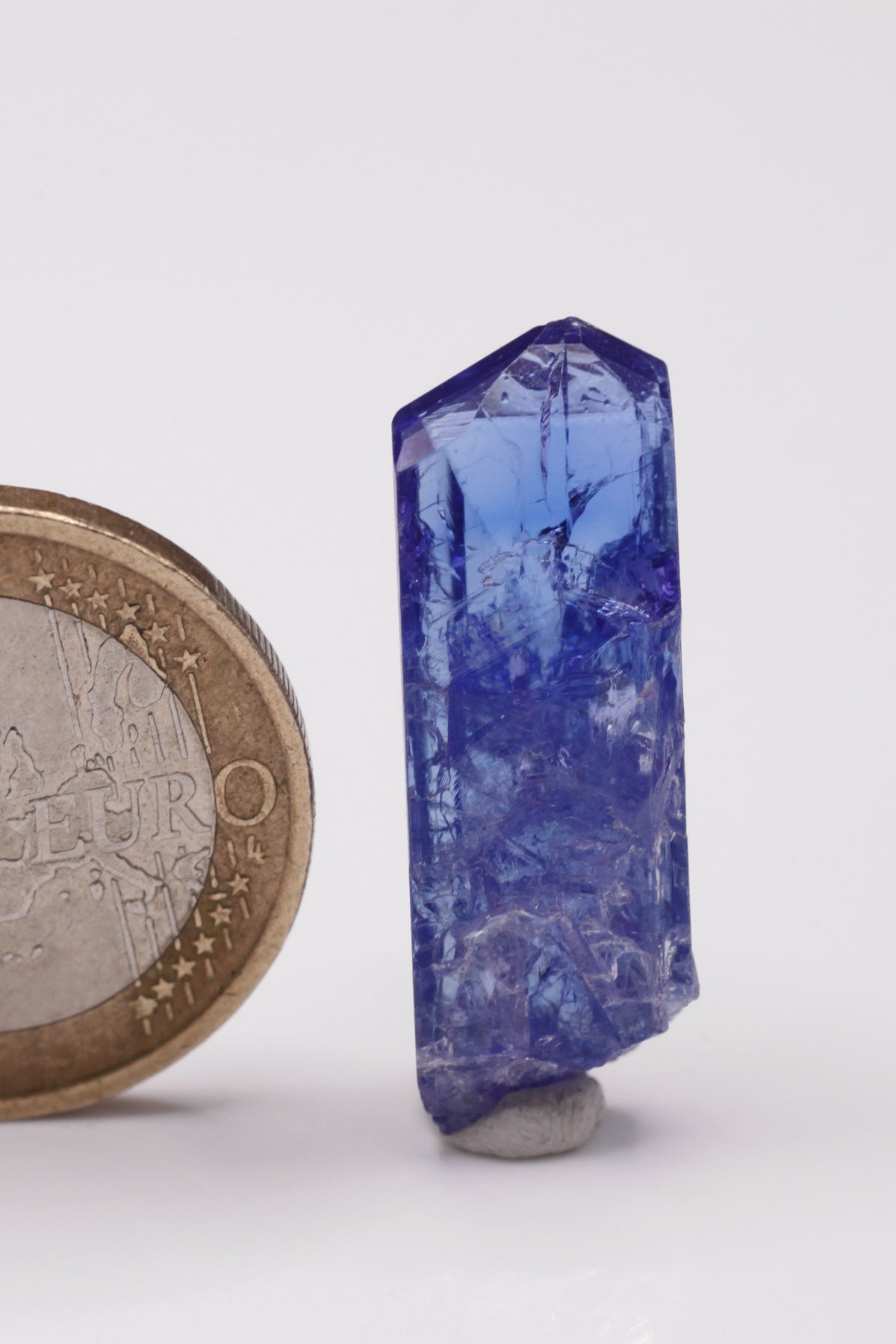 Tanzanite  - Mine Mineral Market :    A033 Dieser schön transparente Kristall war auf einer Seite beim Wachstum eingeengt und bildete deshalb lokal bizarre Prismenflächen aus. Er zeigt dunkelblaue Farbe, sehr gute Endflächen und ebenfalls guten Glanz.  