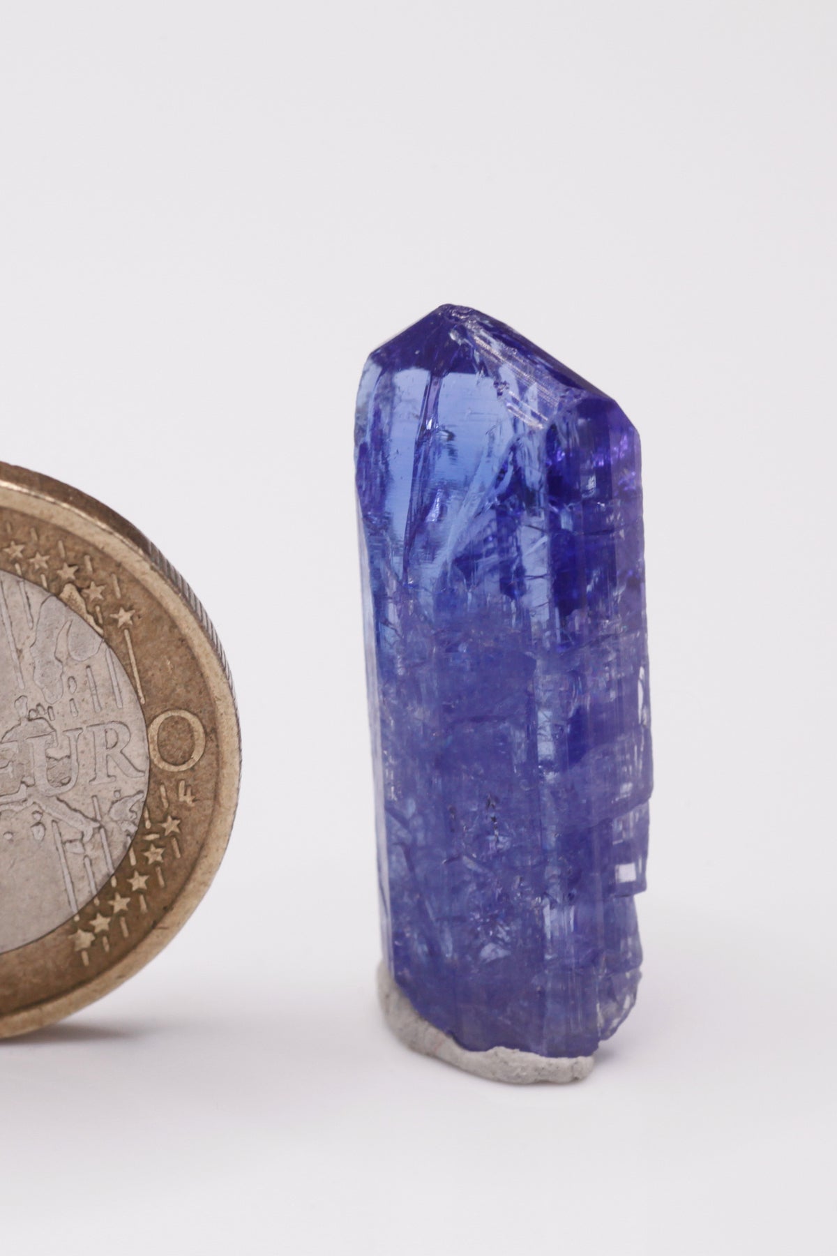 Tanzanite  - Mine Mineral Market :    A033 Dieser schön transparente Kristall war auf einer Seite beim Wachstum eingeengt und bildete deshalb lokal bizarre Prismenflächen aus. Er zeigt dunkelblaue Farbe, sehr gute Endflächen und ebenfalls guten Glanz.  