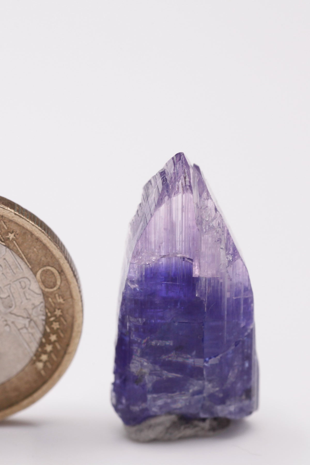 Tanzanite  - Mine Mineral Market :    A034 Ein unbeschädigter kompletter Kristall mit deutlicher Farbzonierung; auf eine hellere Basis folgt ein dunkelblauer Streifen und schließlich eine rosa Spitze.  