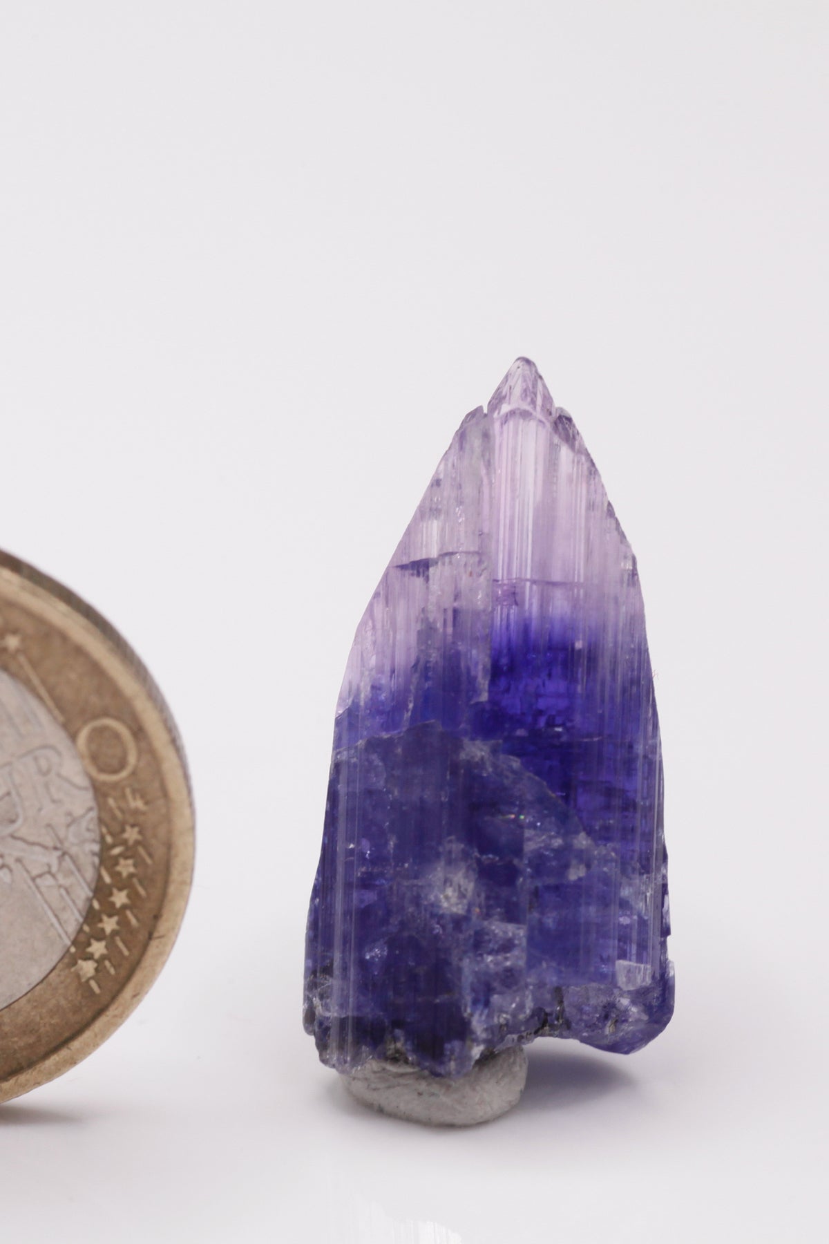 Tanzanite  - Mine Mineral Market :    A034 Ein unbeschädigter kompletter Kristall mit deutlicher Farbzonierung; auf eine hellere Basis folgt ein dunkelblauer Streifen und schließlich eine rosa Spitze.  