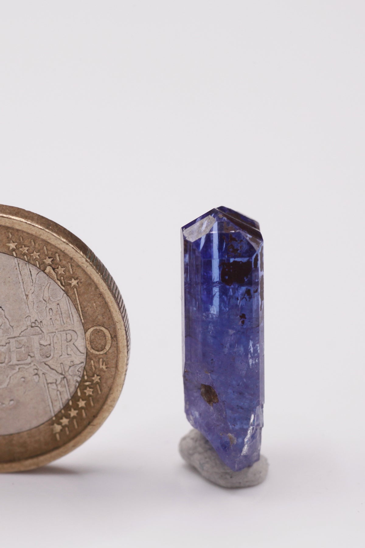 Tanzanite  - Mine Mineral Market :    A035 Ein vollständiger klarer Kristall (im oberen Teil von Facettierqualität) mit hervorragenden Endflächen, auf der Rückseite teilweise mit Alabandin überzogen, sonst sehr guter Glanz.  