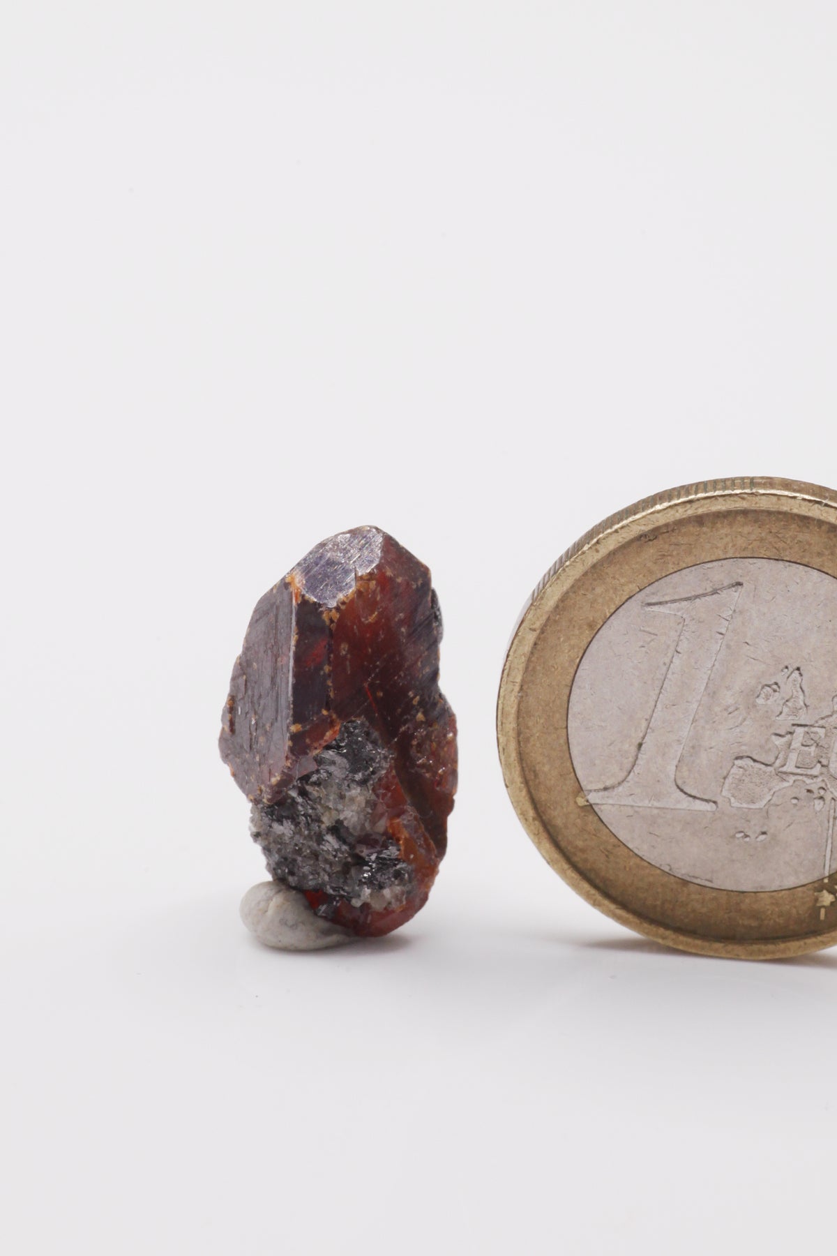 Wurtzite / Sphalerite  - Mine Mineral Market :    A129 Kleiner, länglicher rotbrauner Sphalerit, teilweise mit sehr gut ausgebildeten glänzenden (End-) Flächen. Unten etwas Matrix anhaftend.  