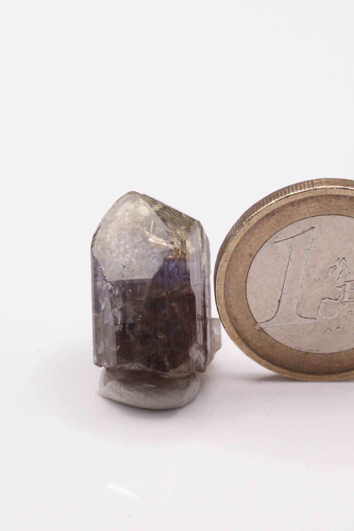 Tanzanite  - Mine Mineral Market :    A232 Wir erhielten ein Tansanitlot aus Altbeständen eines sightholders der seit 2015 geschlossenen Tanzanite One mining Gesellschaft. Dieser gut glänzende Kristall ist zweifarbig, oben gelb und in der Mitte klassisch grau bzw. blauviolett. An der Seite etwas Graphit und Diopsid sowie eine Beschädigung.  