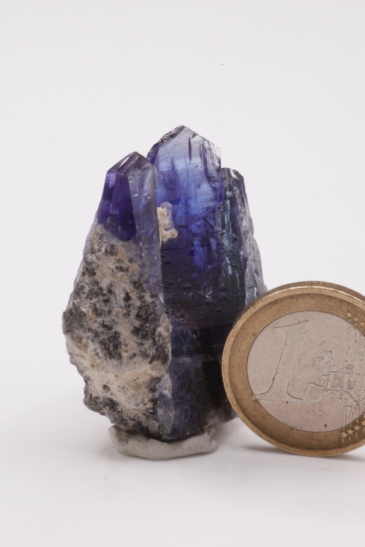 Tanzanite  - Mine Mineral Market :    A234 Zwei kräftig blaue Tansanite, etwas versetzt voneinander zusammengewachsen, bilden so eine sehr ansprechende Tansanit-Stufe. Die Spitzen sind bis auf eine kleine Beschädigung seitlich an der breiteren Spitze vollständig. Guter Glanz, seitlich unten Matrixanhaftungen.  