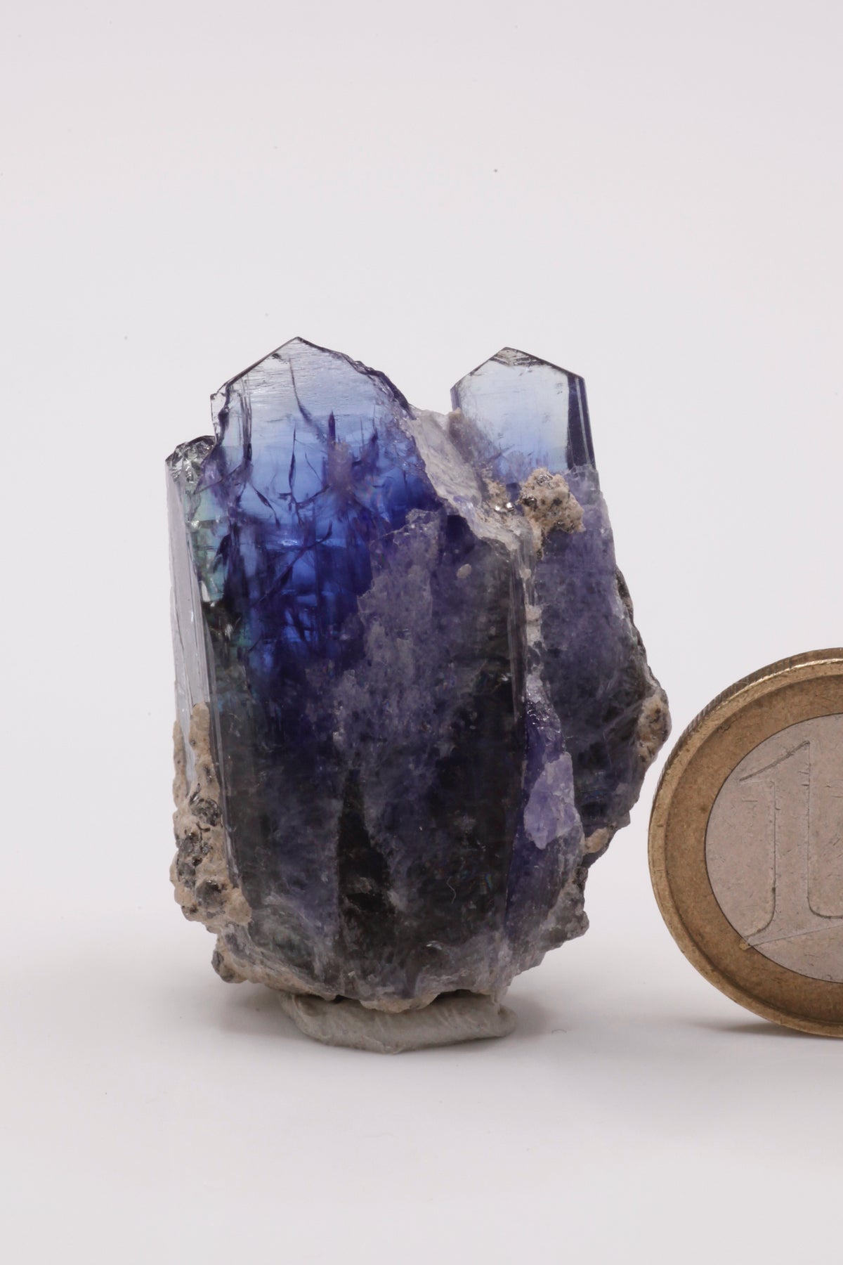 Tanzanite  - Mine Mineral Market :    A234 Zwei kräftig blaue Tansanite, etwas versetzt voneinander zusammengewachsen, bilden so eine sehr ansprechende Tansanit-Stufe. Die Spitzen sind bis auf eine kleine Beschädigung seitlich an der breiteren Spitze vollständig. Guter Glanz, seitlich unten Matrixanhaftungen.  